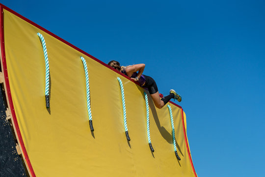Female athlete climbs up a half pipe at an obstacle course race