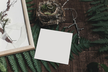 wedding invitation mock-up and rustic boutonniere and wedding rings in bird nest on wooden  background with fern leaves. rustic barn wedding concept. top view. empty card