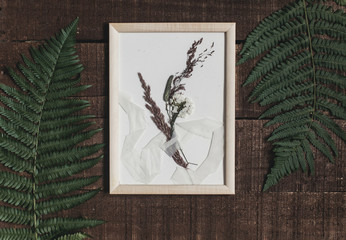 rustic boutonniere under glass in frame on wooden rustic background with fern leaves. barn wedding concept. top view.