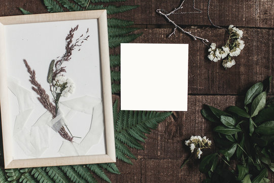 wedding invitation mock-up and rustic boutonniere under glass frame on wooden  background with fern leaves. rustic barn wedding concept. top view. flat lay, empty card