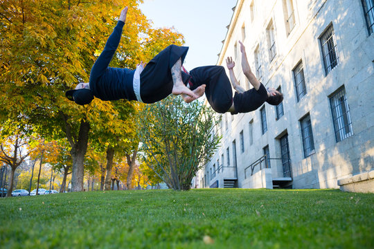 Two young men doing a side flip or somersault while they practicing parkour on the street. 