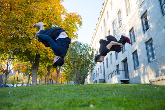Two young men doing a side flip or somersault while they practicing parkour on the street. 