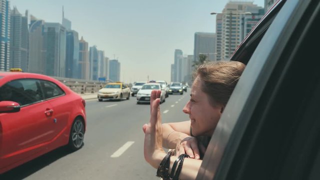 A happy girl sits on the back seat of a car and travels around the city of Dubai.