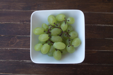 green grapes in a white bowl on a wooden table seen from above