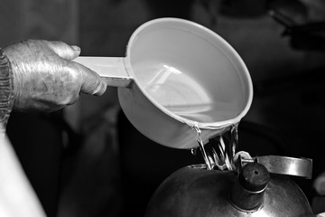 the old man pours water from a bucket into a kettle, black and white photo
