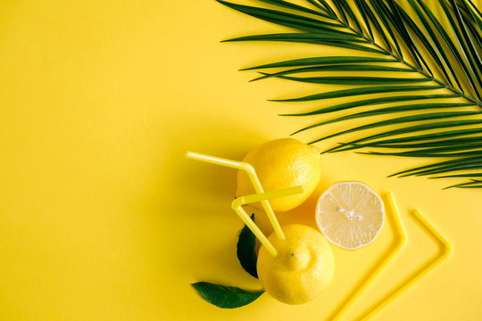 Summer background. Lemon refreshing drink with straw. Tropical palm leaves, lemon on a yellow background. Flat lay, top view, copy space 