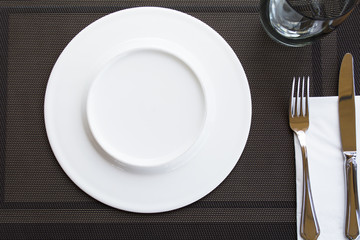 White empty plates with fork and knife tied with a ribbon on a brown tablecloth