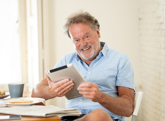 Handsome senior retired old man using tablet with joy while having breakfast at home
