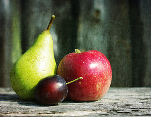 Ripe green pears, red apples and plum on a wooden surface with grunge texture, close up. 