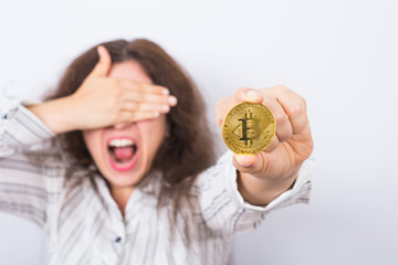 Problems in economics - Shocked businesswoman closes her eyes with her hand and holding golden bitcoin on white background