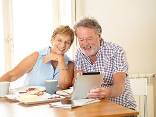 Beautiful senior retired old couple using digital tablet with joy while having breakfast at home
