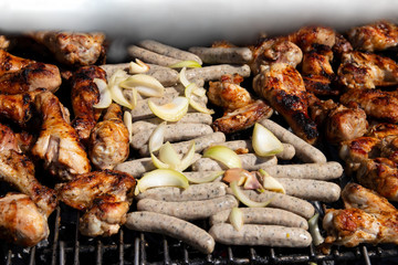 Chicken meat and sausages with onions over the coals on a barbecue. Concept food. Close up.