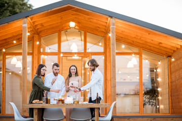 Four friends enjoying evening time having a dinner on the backyard of the modern country house outdoors