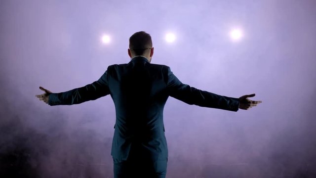 showman presents his show, spreading his hands to the sides. The guy in the purple camisole and the cylinder. Bright tailcoat, suit. Rear view of a male public speaker speaking at the microphone