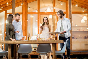 Friends having a dinner with pizza on the backyard of the modern house decorated with lights during the evening time outdoors
