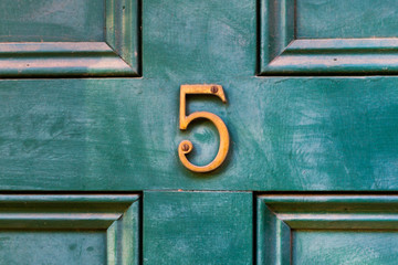 House door number 5 in bronze on an older wooden painted green door