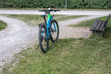 Fototapeta premium Fahrrad steht auf Kiesweg, Weggabelung mit Bank