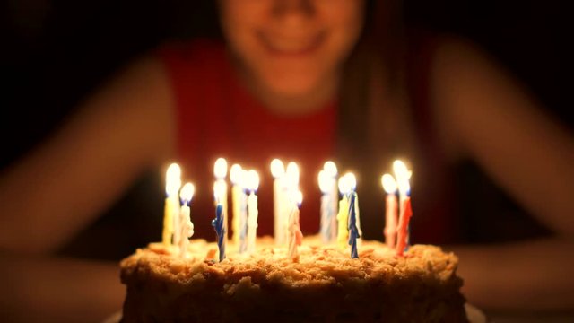 Happy cheerful young celebrating birthdaywith cake at home in evening. Birthday girl make wishes and blowing out candles. Focus on the cake