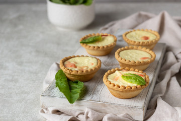 Mini tartlets with cream cheese filling and salmon on white wooden cutting board.