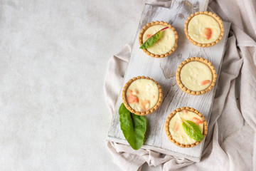 Mini tartlets with cream cheese filling and salmon on white wooden cutting board.