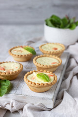 Mini tartlets with cream cheese filling and salmon on white wooden cutting board.