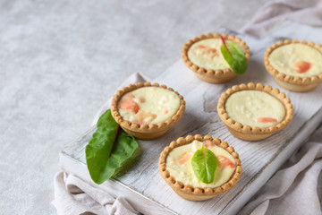 Mini tartlets with cream cheese filling and salmon on white wooden cutting board.
