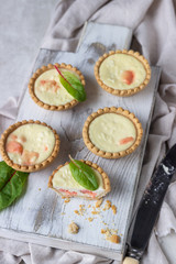 Mini tartlets with cream cheese filling and salmon on white wooden cutting board.