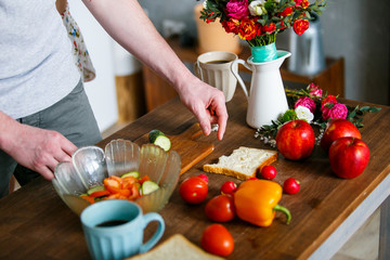 Young man making healthy breakfast. Ripe vegetables and apples on wooden table