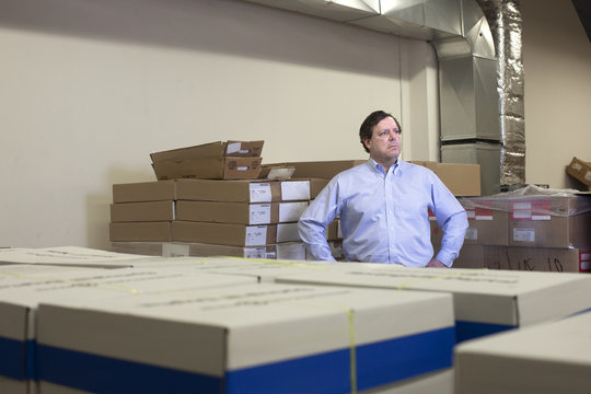 Business owner standing inside office warehouse with piles of business supplies around him