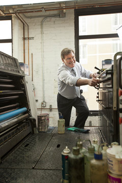 Business owner smiling and working with industrial printing machines inside an office in New York City, USA