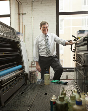 Business owner smiling and standing in front of industrial printing machines inside an office in New York City, USA