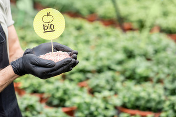 Farmer holding bio fertilizers with green plants on the background, close-up view