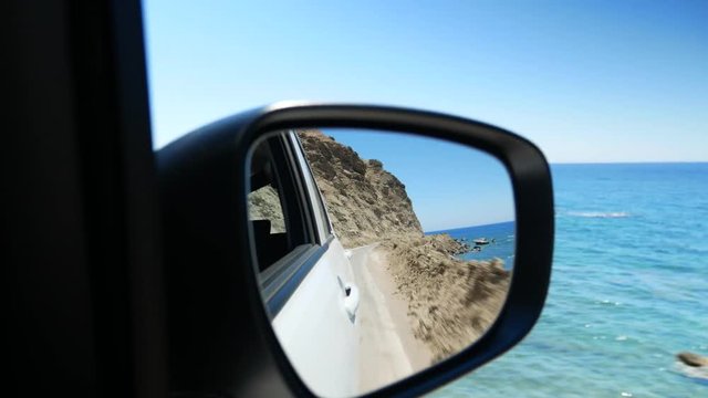 Driving along the sea side road and watching the coastline in the rear-view mirror