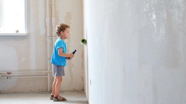 Curly hair baby boy painting the wall with a roller