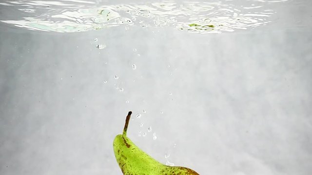 One pear of variety conference falls into the water with bubbles in slow motion. Fruits isolated on a white background.
