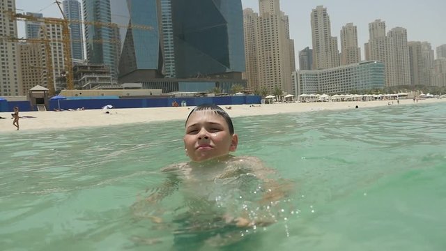 Portrait of a ten-year-old boy suffering from heat and swimming in the light green sea with sandy coast in Dubai on a sunny day in summer.