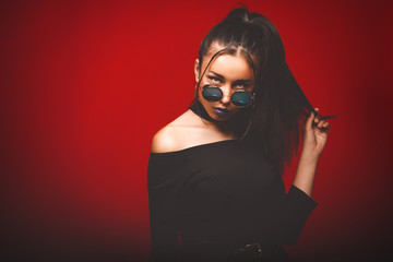Portrait of cool crazy brunette fashionable girl in sunglasses, casual hairdo on red background. Woman like bitch with pretty makeup big lips