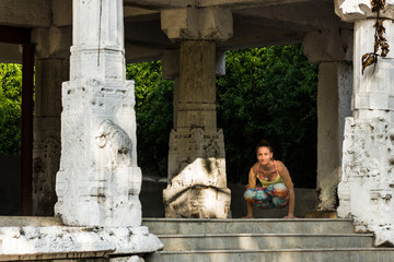 Woman practicing yoga in utpluthih pose in temple between columns with sculptures carved in Srirangapatna temple, Karnataka, India. Female yogi keeping balance on two hands