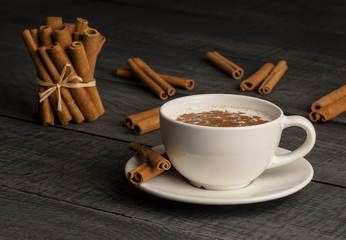 Close up white cup of salep milky hot drink of Turkey with cinnamon powder healthy spice on black wooden background
