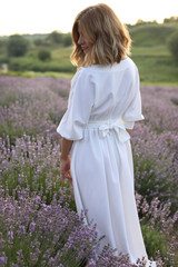 Fototapeta na wymiar rear view of attractive woman in white dress standing in violet lavender field