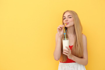 Young woman with glass of delicious milk shake on color background