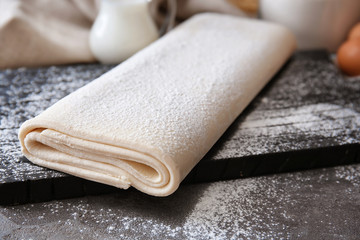 Wooden board with raw flaky dough on table