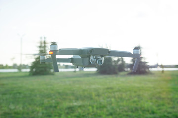Fototapeta premium Flying quadcopter drone with Action Camera in the park under blue sky with lens flare.
