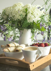 Coffee, rugelach with chocolate filling, strawberries and flowers on wooden tray.