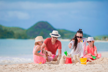 Family making sand castle on white beach on summer holidays