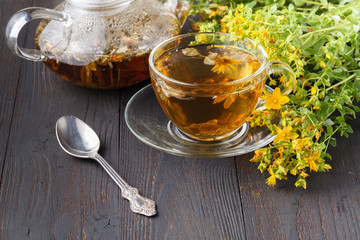 Glass teapot and cup with green tea on old wooden table with fresh herbs