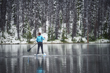 a woman paddle boarding on a mountain lake in the winter
