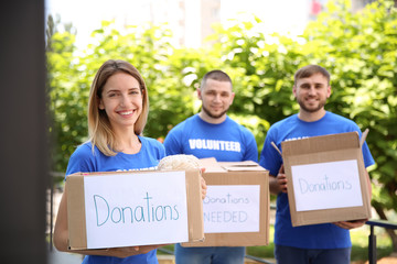 Young volunteers holding boxes with donations for poor people outdoors