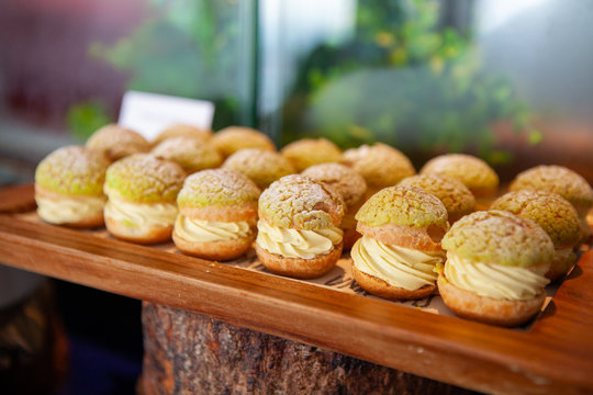 Tasty Mini Green Tea Choux au Craquelin or French Crunchy Cream Puff filled with delicious and creamy Chantilly Cream on a wooden tray. Selective focus.