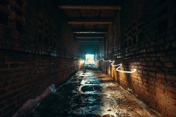Light and exit in end of dark long brick abandoned industrial tunnel or corridor or sewer channel,...